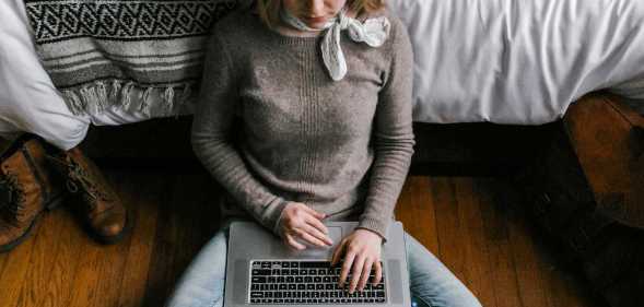 Girl sits on the floor with a laptop over her legs.
