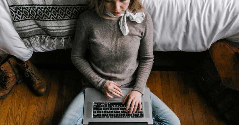 Girl sits on the floor with a laptop over her legs.