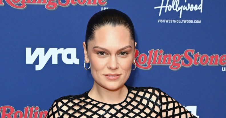 Jessie J posing on red carpet, hair pulled back, wearing silver hoop earrings and black sequin fishnet top.