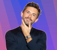 Jonathan Bailey smiles and places his hand on his chin. He is against a multi-coloured background.