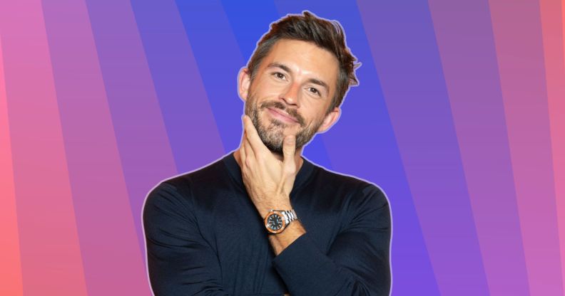 Jonathan Bailey smiles and places his hand on his chin. He is against a multi-coloured background.