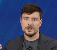 Mr Beast wearing a grey suit while speaking on a panel against a dark blue backdrop