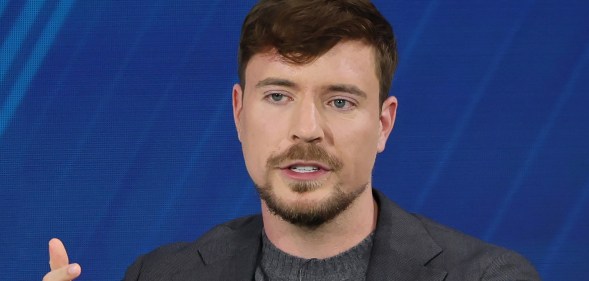Mr Beast wearing a grey suit while speaking on a panel against a dark blue backdrop