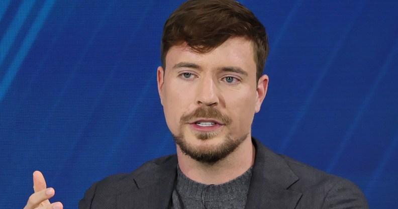 Mr Beast wearing a grey suit while speaking on a panel against a dark blue backdrop