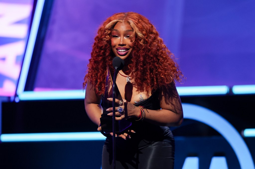 SZA accepting an award on stage in an all-black dress