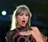 Taylor Swift performs onstage during the Eras tour. She's looking shocked with her hand on her chest.