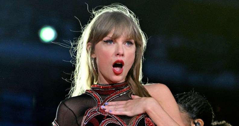 Taylor Swift performs onstage during the Eras tour. She's looking shocked with her hand on her chest.