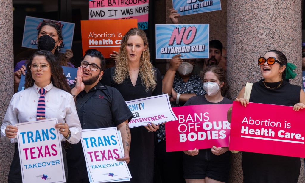 A crowd of protestors holding pro-trans signs outside of a building.