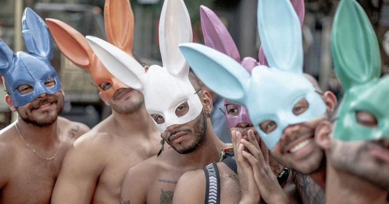 A group of shirtless men at a Pride event wearing multicoloured rabbit ears.