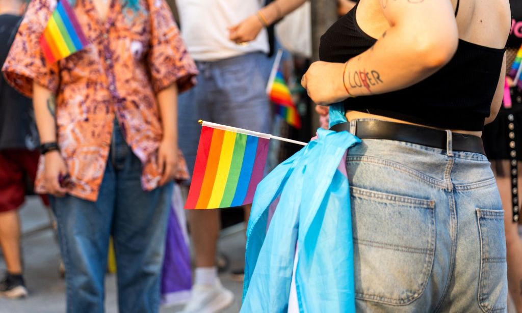 An anonymous person tying a trans flag to their belt during a Pride protest.