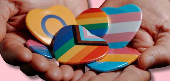 Hands held out hold LBGTQ+ badges.