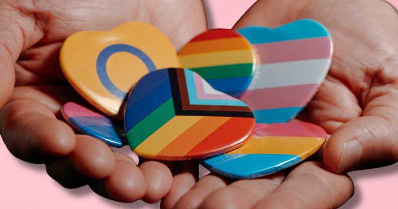 Hands held out hold LBGTQ+ badges.