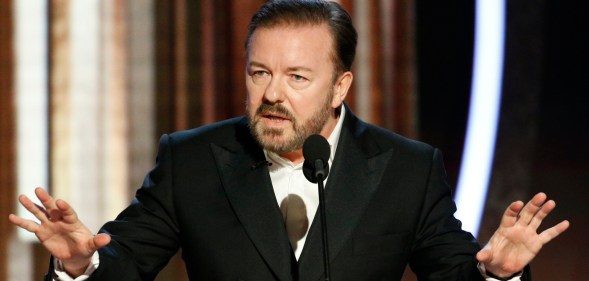 Ricky Gervais speaking into a mic with his hands up