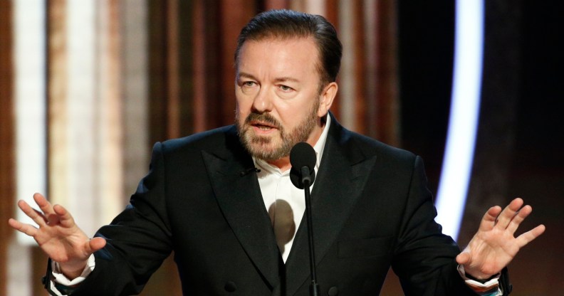 Ricky Gervais speaking into a mic with his hands up