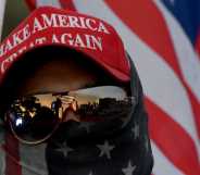 A man wearing a MAGA hat and carrying a flag protests during a pro Trump rally.