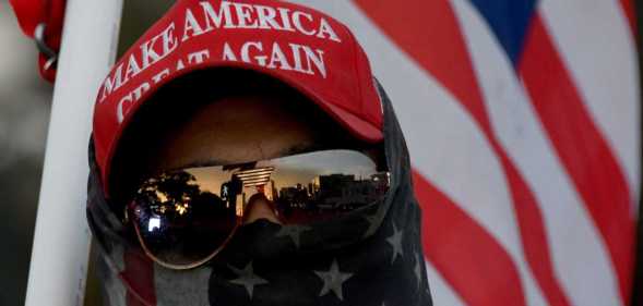 A man wearing a MAGA hat and carrying a flag protests during a pro Trump rally.