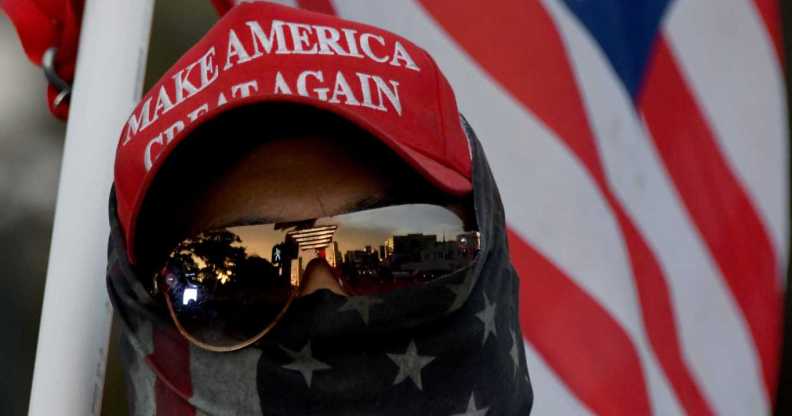 A man wearing a MAGA hat and carrying a flag protests during a pro Trump rally.