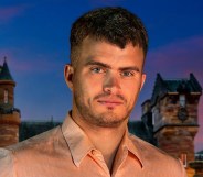 Matthew stood in front of The Traitors castle in a light pink shirt