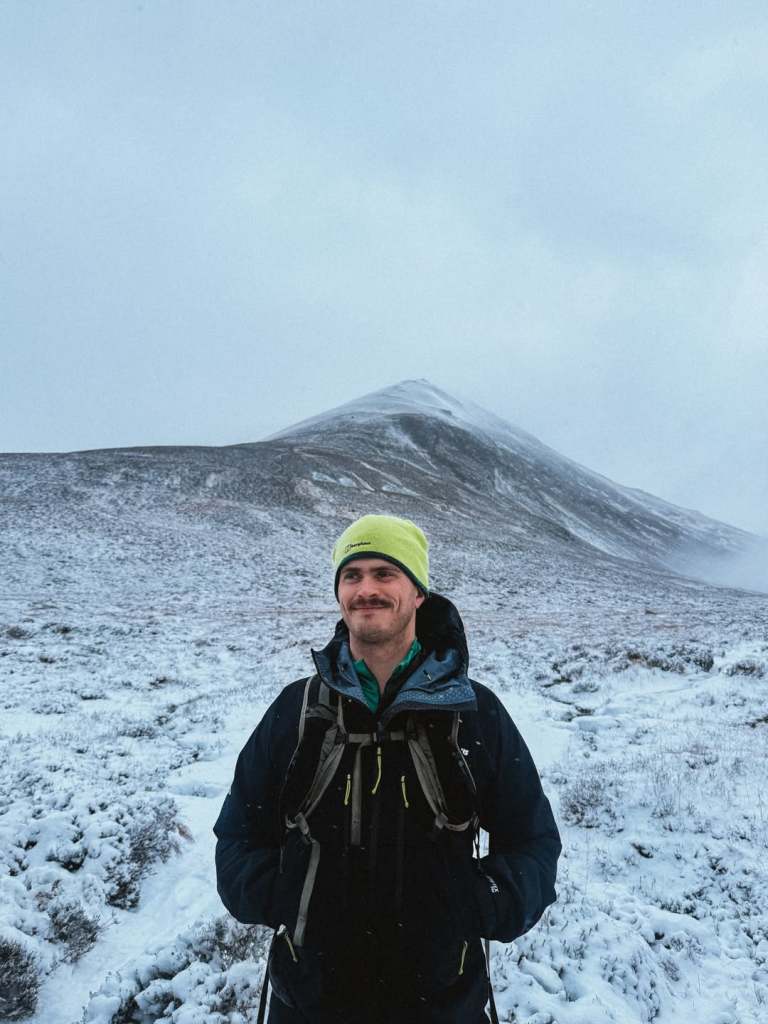 Matthew wearing a neon beanie and hiking gear against a snowy hill backdrop