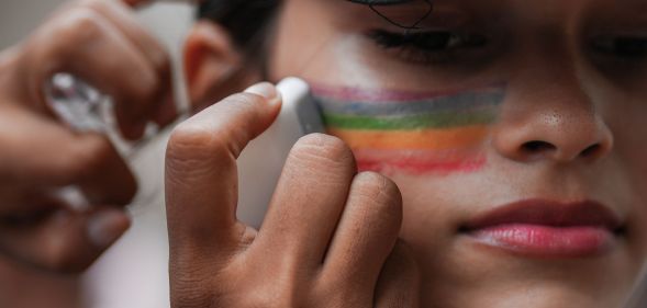 A close-up of someone putting rainbow face paint on their cheek.