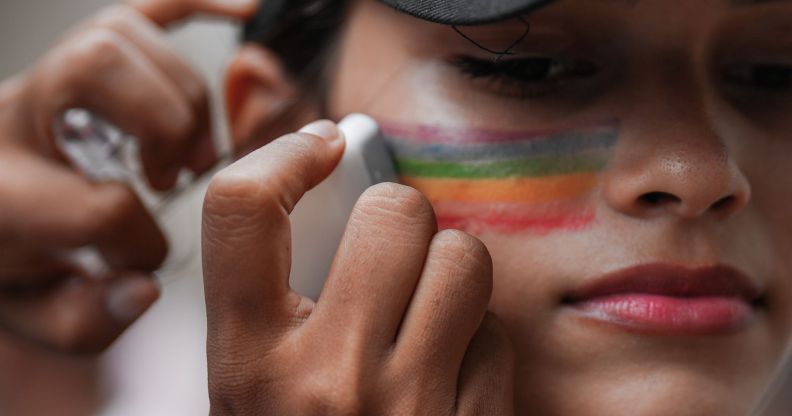 A close-up of someone putting rainbow face paint on their cheek.