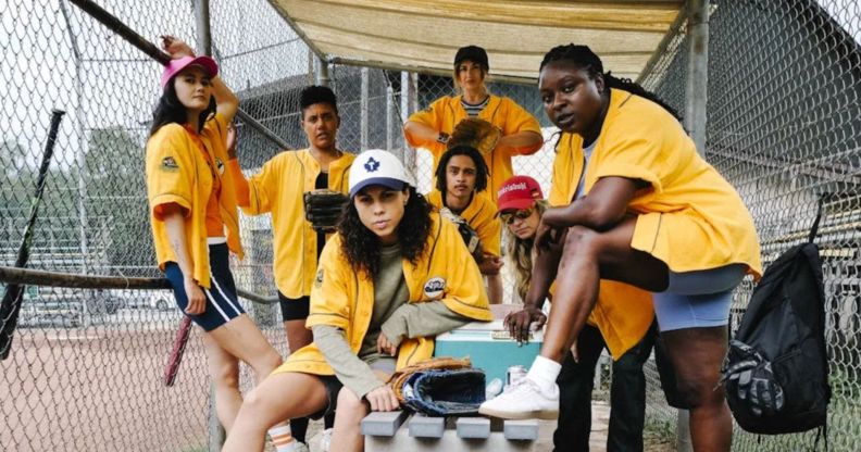 A first look still from upcoming show Slo Pitch showing softball players posing in yellow tops, posing by a pitch, looking at the camera.