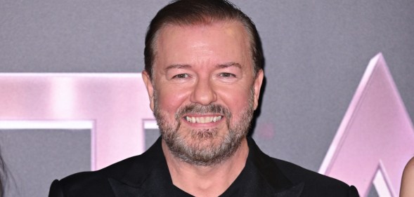 Ricky Gervais in all black suit smiling at the camera