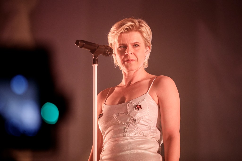 Robyn performing with a white vest dress top