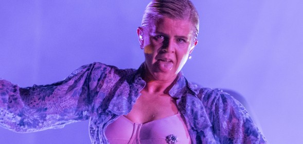 Robyn performing with a floral shirt open to reveal a bejewelled bra