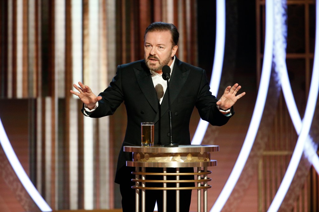 Ricky Gervais speaking into a mic with his hands up