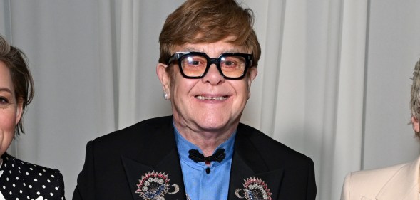 Elton John wearing a blue shirt and black suit jacket with floral embroidery