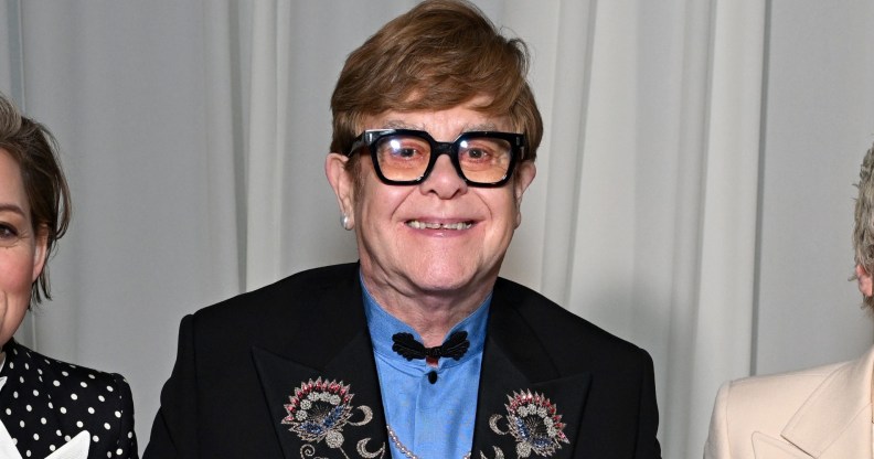 Elton John wearing a blue shirt and black suit jacket with floral embroidery