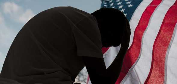 A distressed man in silhouette sits in dark room texting on smartphone. Blinds drawn in window light making silhouette of man with hand of forehead communicating on cell phone. Moody dark image with copy space.