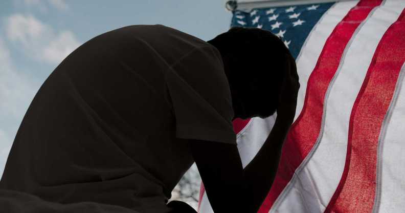 A distressed man in silhouette sits in dark room texting on smartphone. Blinds drawn in window light making silhouette of man with hand of forehead communicating on cell phone. Moody dark image with copy space.