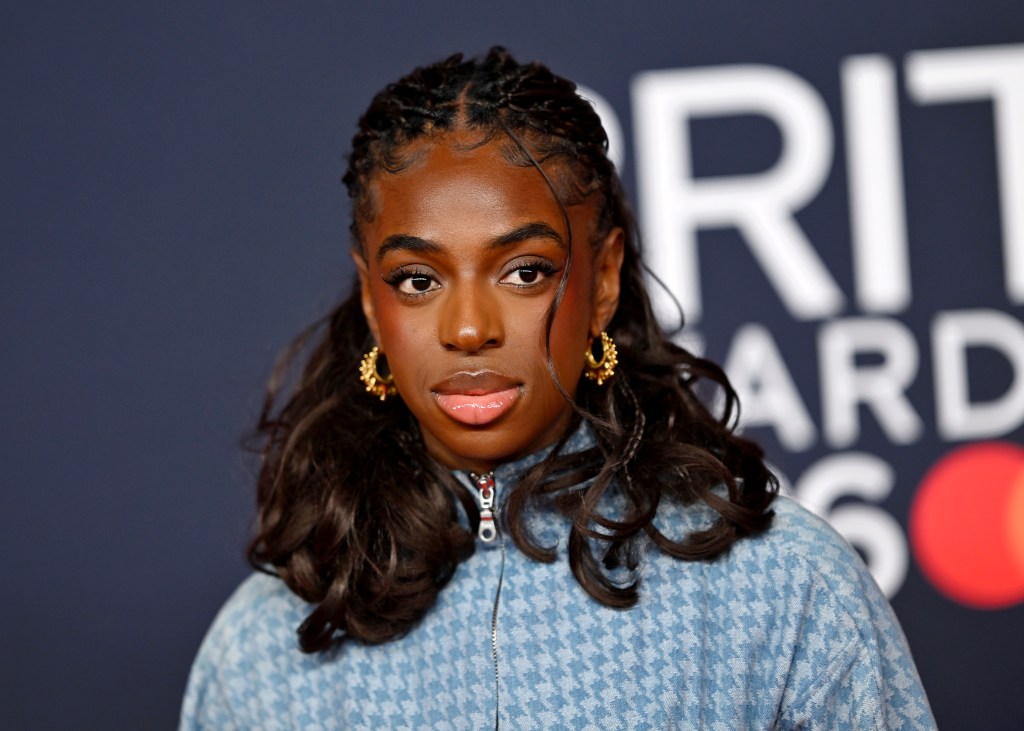 Cat Burns attends The BRIT Awards 2026 with a denim blue jacket and gold hoop earrings.