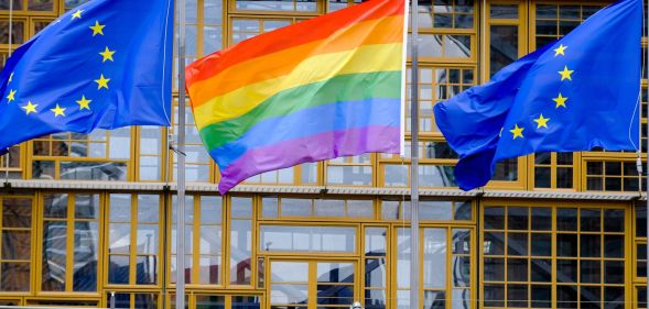 An LGBTQ+ Pride flag in between two European Union flags.