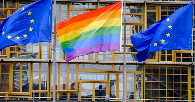 An LGBTQ+ Pride flag in between two European Union flags.