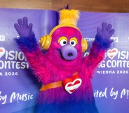 Auri is the mascot of the 2026 Eurovision Song Contest. A fluffy creature which has a pink head that fades to purple and then blue legs. Auri is wearing trainers and has yellow headphones on. Holiday Austria flag heart