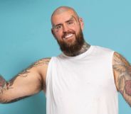 Handcuffed contestant Rob smiling wearing handcuffs while against a blue background.