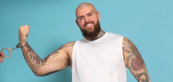 Handcuffed contestant Rob smiling wearing handcuffs while against a blue background.