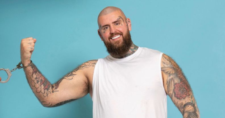 Handcuffed contestant Rob smiling wearing handcuffs while against a blue background.