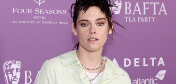 Kristen Stewart in a pale yellow shirt and two silver chain necklaces against a purple BAFTA backdrop