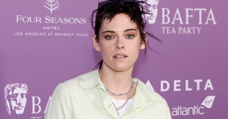 Kristen Stewart in a pale yellow shirt and two silver chain necklaces against a purple BAFTA backdrop