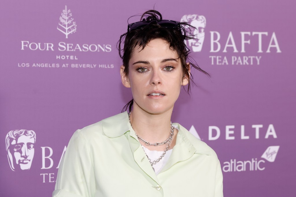 Kristen Stewart in a pale yellow shirt and two silver chain necklaces against a purple BAFTA backgrop