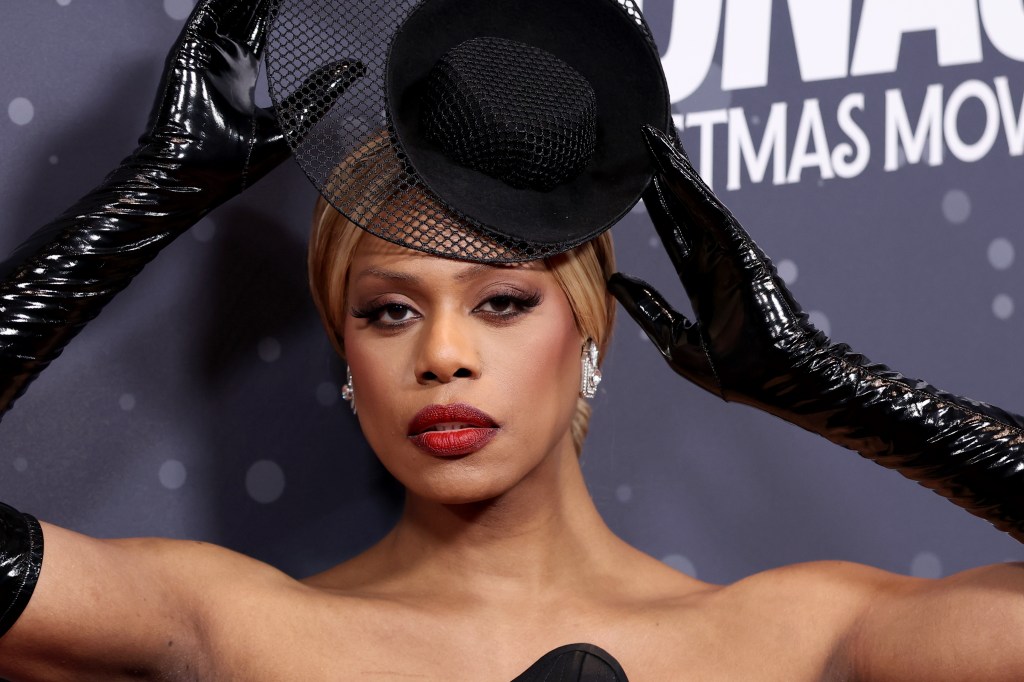 Laverne Cox wearing a black dress, black leather gloves and lacy black hat