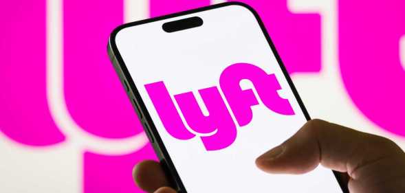 In this photo illustration, a smartphone displays the logo of Lyft Inc. (NASDAQ: LYFT), a major American ride-sharing company, with a blurred version of the company's pink logo visible in the background.