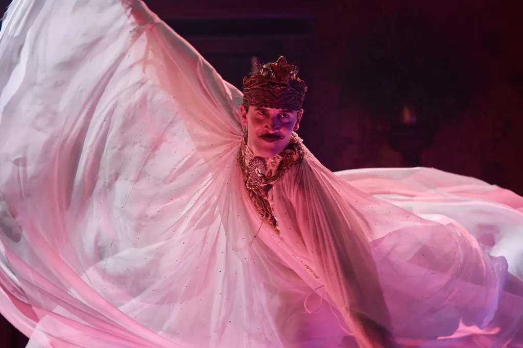 Madfabulous still: Callum Scott Howells wearing a crown, draped in white fabric in pink light as he spins