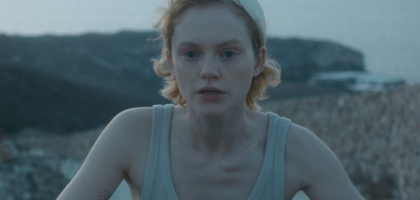 Satisfaction's Emma Laird as Lola, cycling in a vest top by the beach