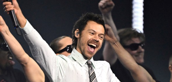 Harry Styles performs 'Aperture' on stage during The BRIT Awards. He's in a white and grey striped shirt with a grey and black tie.