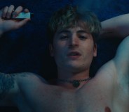 Kieron Moore stars as Aaron. He's topless, lying down and looking up at the camera with a vape in his hand.
